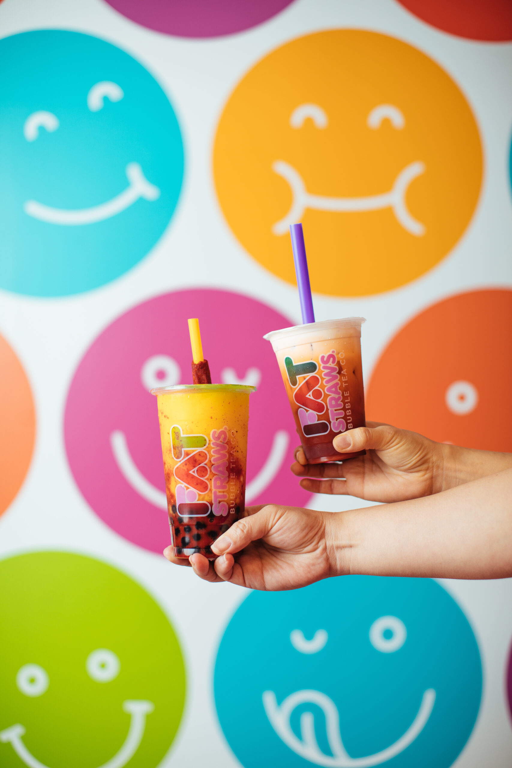 Two Fat Straws drinks held up in front of a colorful store mural
